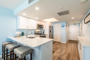 A modern kitchen with white cabinets, a central island with stools, stainless steel appliances, and a blue accent wall.