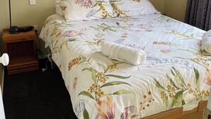 A neatly made bed with floral bedding, a bedside lamp, and a small wooden nightstand with a lamp and a phone. - Cosy cabin (Lumsden)