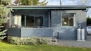 A small, modern house with a large sliding glass door, a covered patio, and two propane tanks. - Cosy cabin (Lumsden)