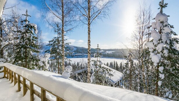 Schneebedeckte Landschaft mit einer Holzterrasse und verschneiten Bäumen.