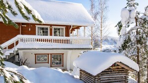 Eine Blockhütte mit Balkon, umgeben von schneebedeckten Bäumen und einem klaren Himmel.