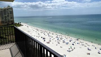 A beach with numerous umbrellas and people, a clear sky, and a building in the background.