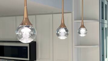 A modern kitchen with white cabinetry, a black microwave, and three spherical pendant lights with a clear glass cover.