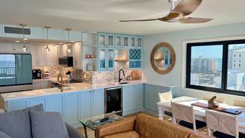 A modern kitchen with blue cabinets, a large window with a city view, and a ceiling fan.