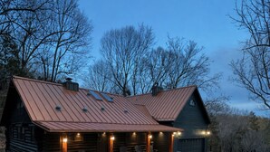 Een rustieke blokhut met een metalen dak, een overdekte veranda met zitplaatsen en een vuurkuil in de tuin.