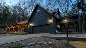 Een groot, donker houten huis met garage, overdekte veranda en terras.
