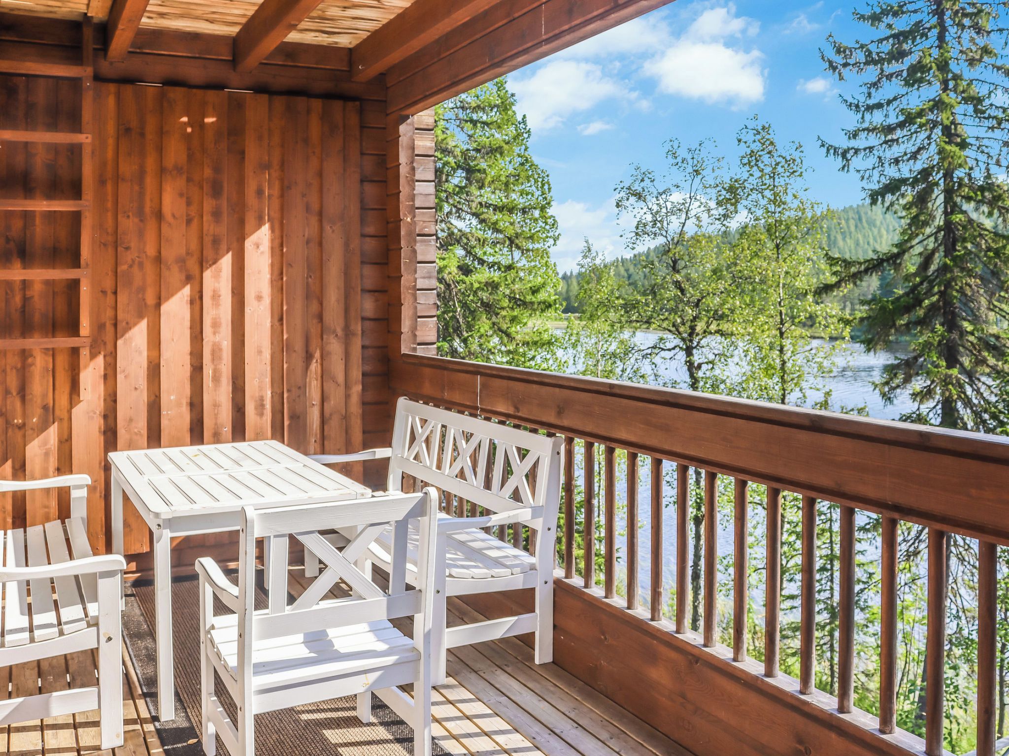 A wooden deck with a table and chairs, overlooking a lake and forest.