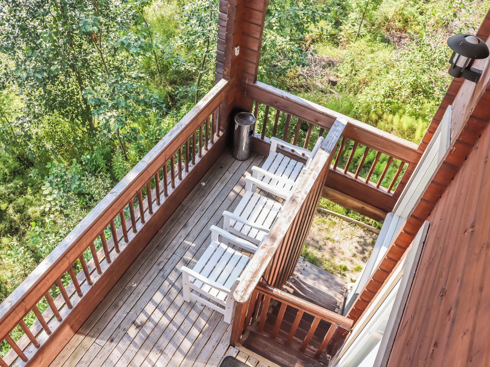 A wooden deck with a metal trash can and two white chairs.