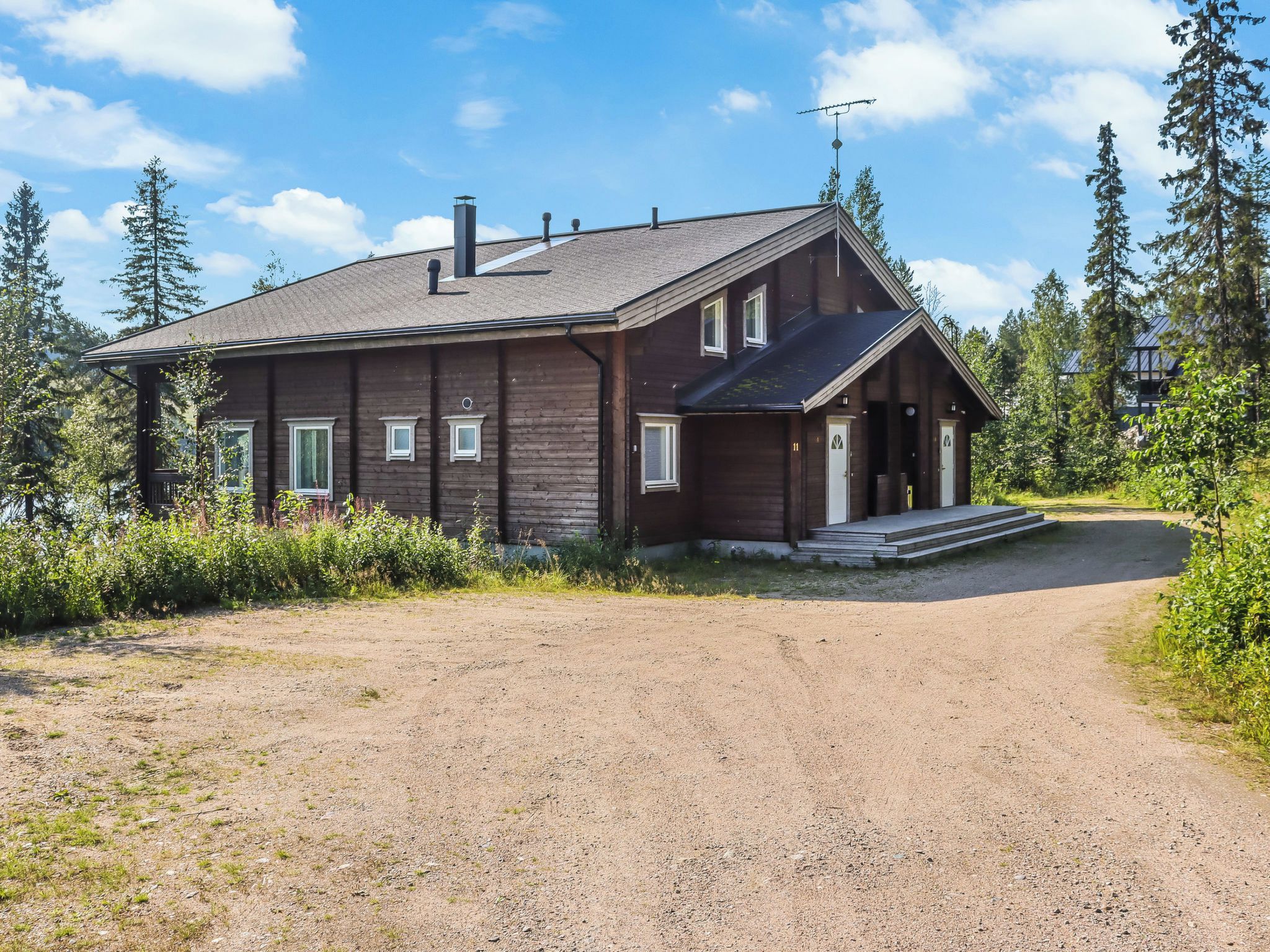 A two-story wooden cabin with a gravel driveway leading to a wooden porch.