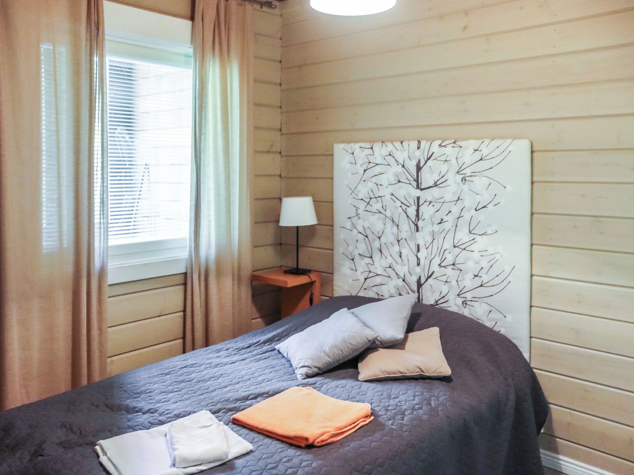 Un dormitorio con cama, mesita de noche, lámpara y una obra de arte en la pared.