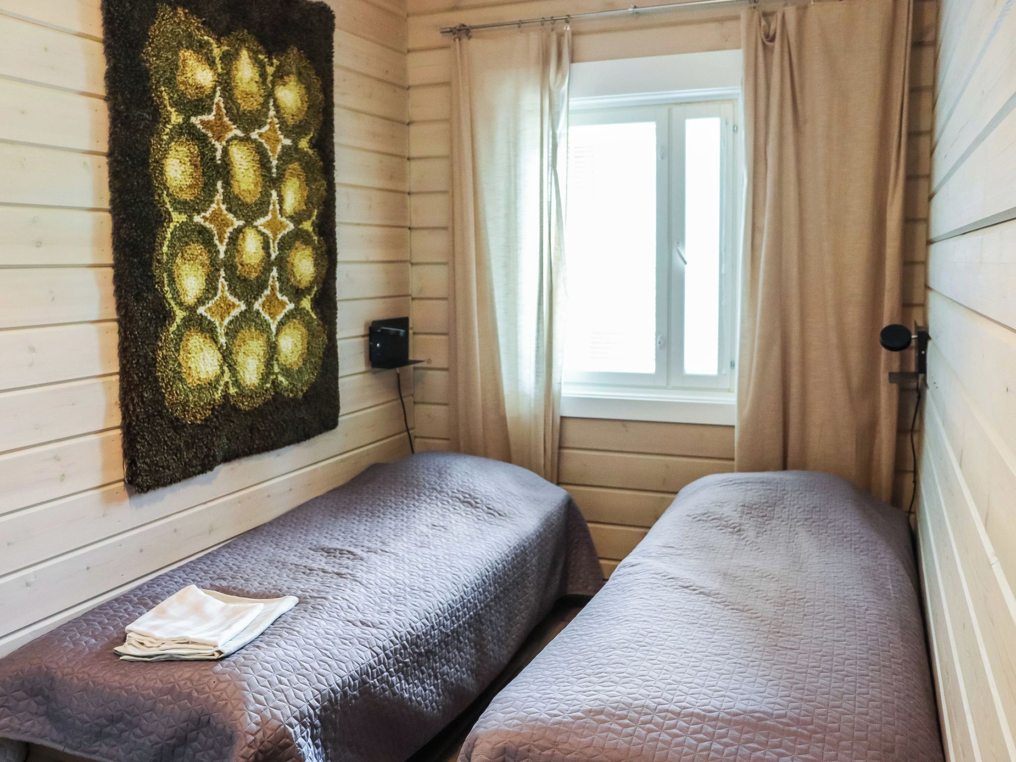 Et værelse med to senge, et vindue med gardiner og en vægmonteret lampe.