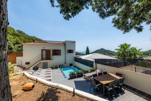 A modern villa with a swimming pool, outdoor seating, and a view of the hills.