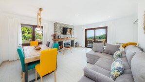 A modern living room with a fireplace, dining area, and large windows. - Vacation Home Sestel with Sea View, Pool, Balcony, Garden & Terrace (Capdepera)