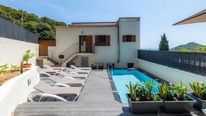 A poolside area with lounge chairs, a pool, and a building with a staircase. - Vacation Home Sestel with Sea View, Pool, Balcony, Garden & Terrace (Capdepera)