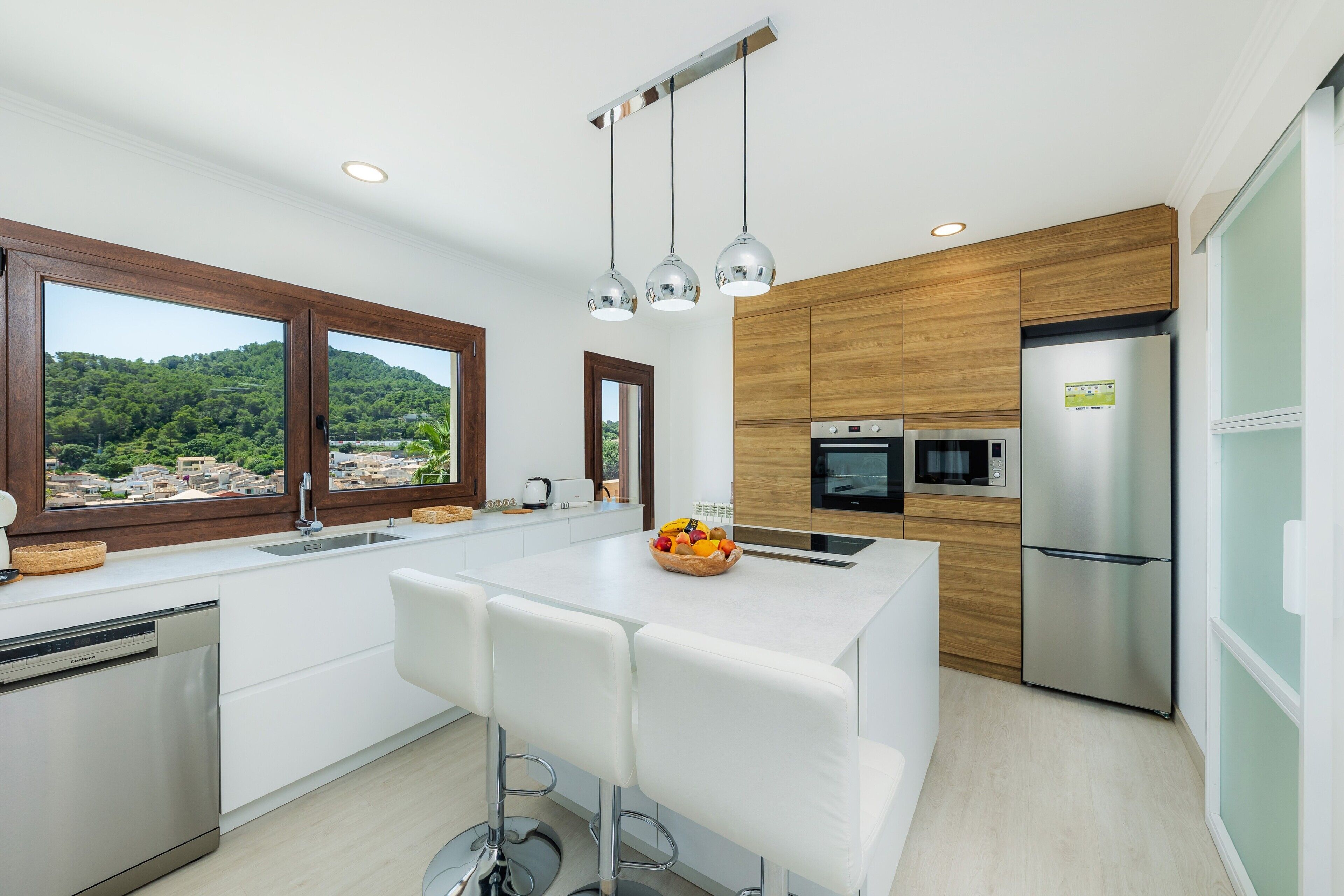 Une cuisine moderne dotée d’un îlot central, d’appareils électroménagers en acier inoxydable et offrant une vue sur un paysage verdoyant.