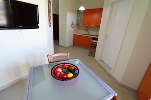 A dining area with a glass table, a bowl of fruit, a television, and orange cabinets in the background. - Holiday Apartment 'Casa Lucia' near the Beach with Air Conditioning and Balcony (Otranto)