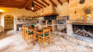 Une cuisine rustique avec des murs en pierre, des poutres en bois, une cheminée et un coin repas avec des chaises.