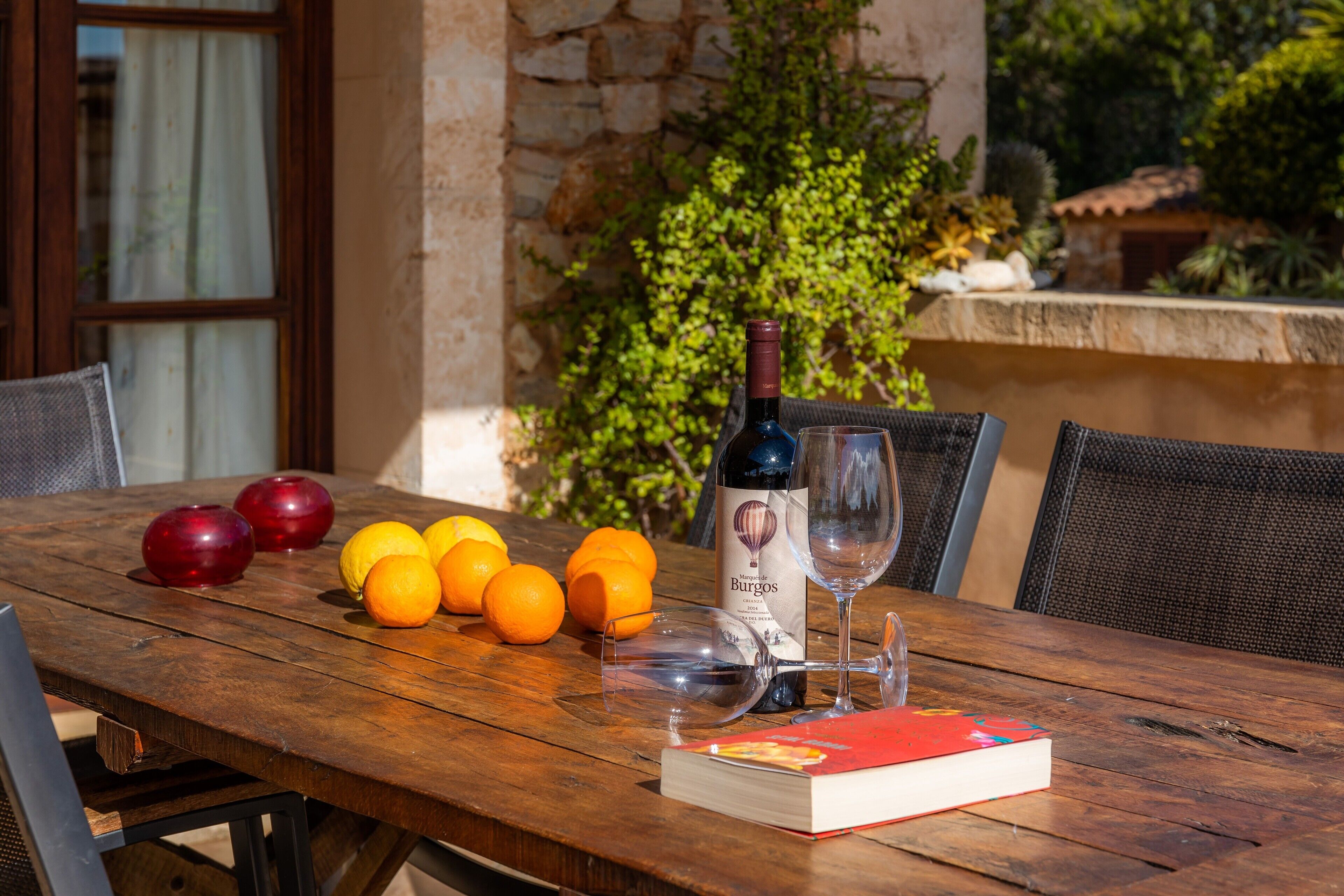 Una mesa de madera con una botella de vino, copas, manzanas y naranjas.