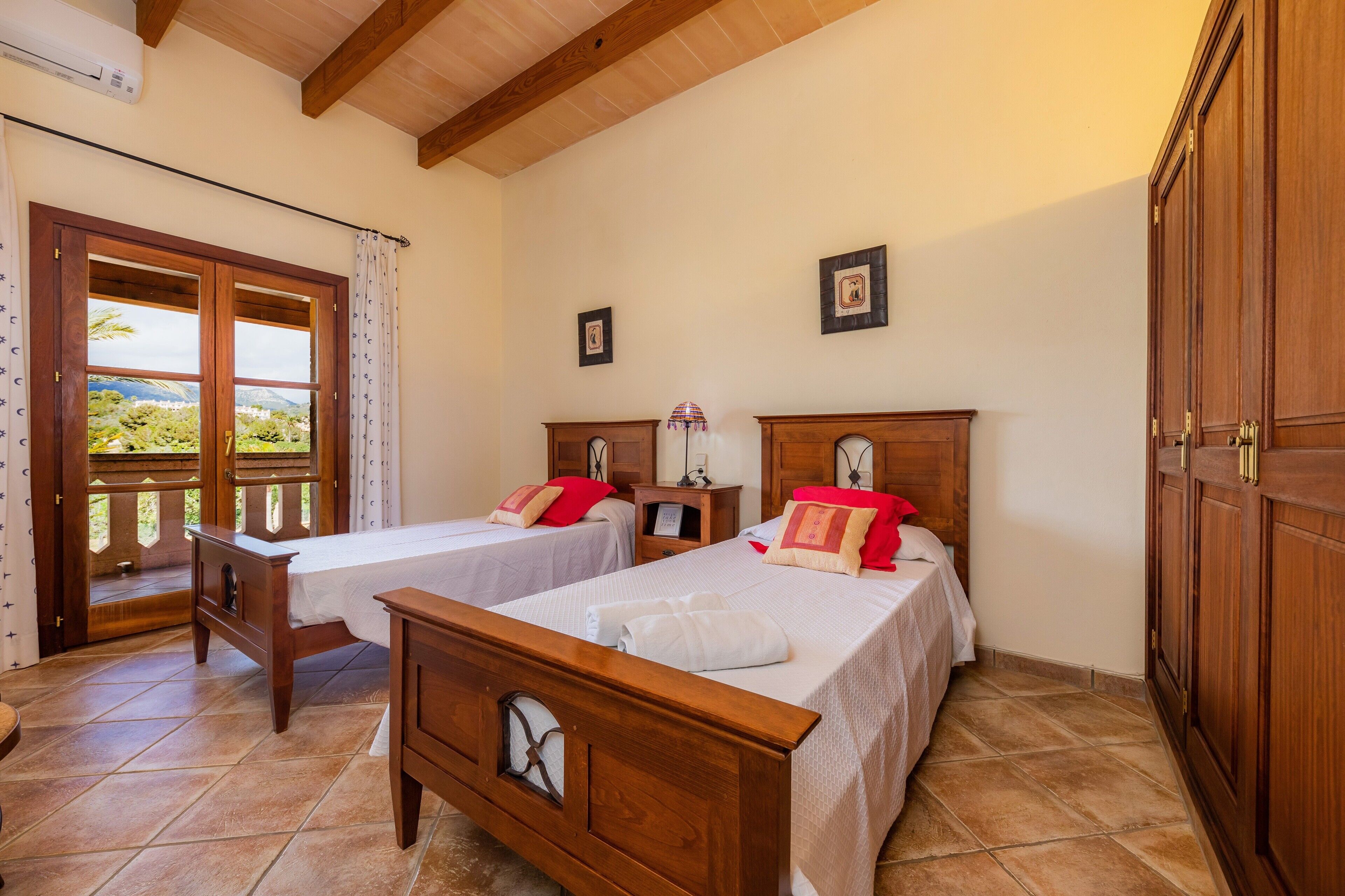 Quarto com duas camas de madeira, um guarda-roupa de madeira, uma janela com vista e uma porta para o exterior.