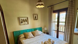 Une chambre à coucher avec un lit, une fenêtre avec des rideaux, une lampe fixée au mur et deux tableaux encadrés.