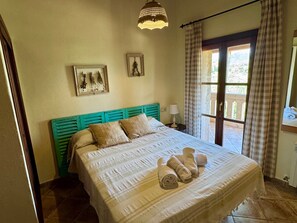 A bedroom with a bed, a window with curtains, a wall-mounted lamp, and two framed pictures.