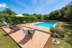 Un jardin avec une piscine, des chaises longues, un espace de jeux pour enfants et un panneau indiquant qu'il est interdit de se baigner.