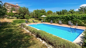 A rectangular swimming pool with a clear blue water surface, surrounded by a stone border. There are four lounge chairs aligned along the pool's edge, and a small gazebo with a white roof is visible in the background. - Pool Suite Glavotok at Krk Island, Krk, Croatia (Krk)