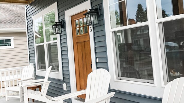 En inglasad veranda med vita Adirondack-stolar och en trädörr som är numrerad med 5.
