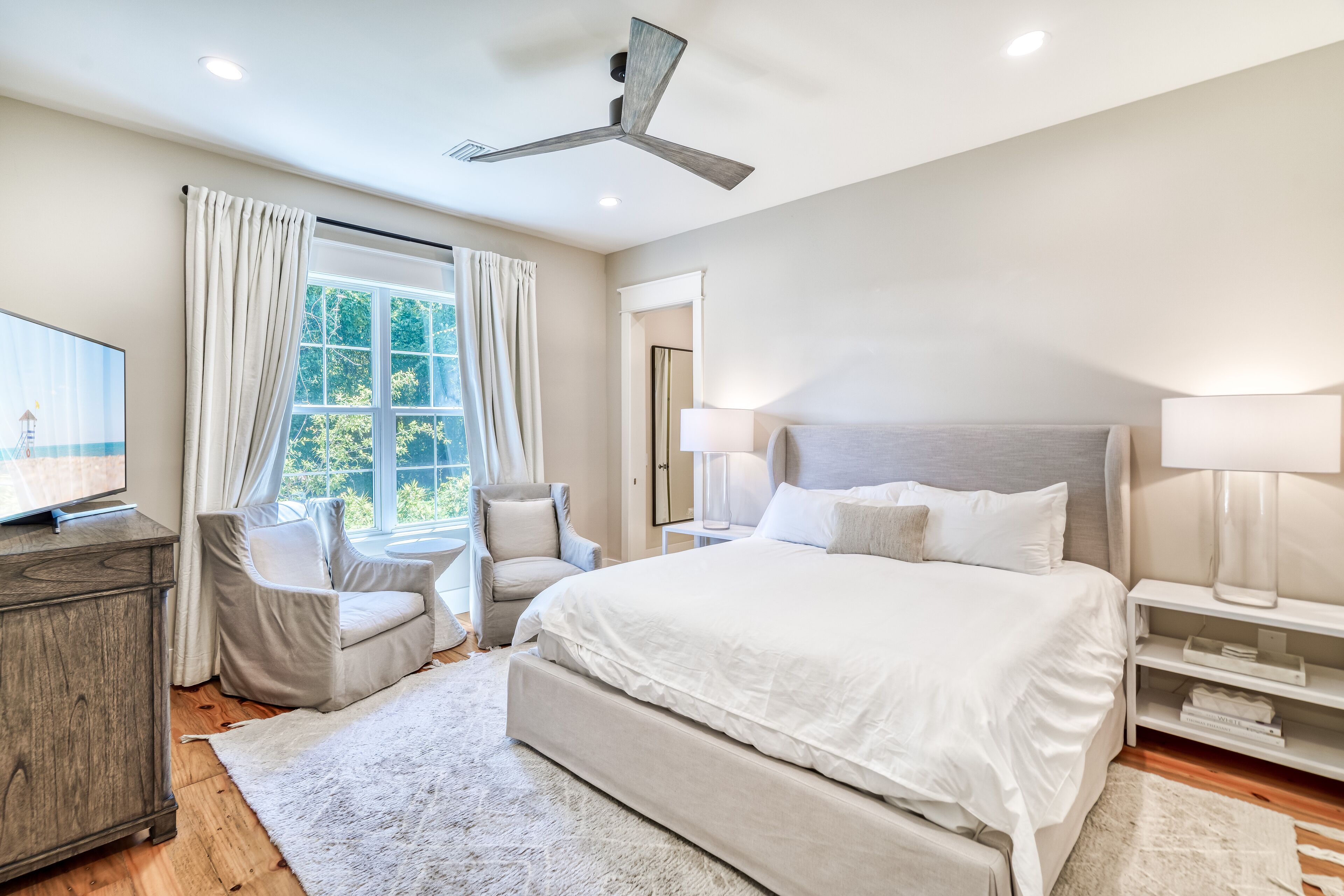A modern bedroom with a large bed, a ceiling fan, a TV, and a window with curtains.