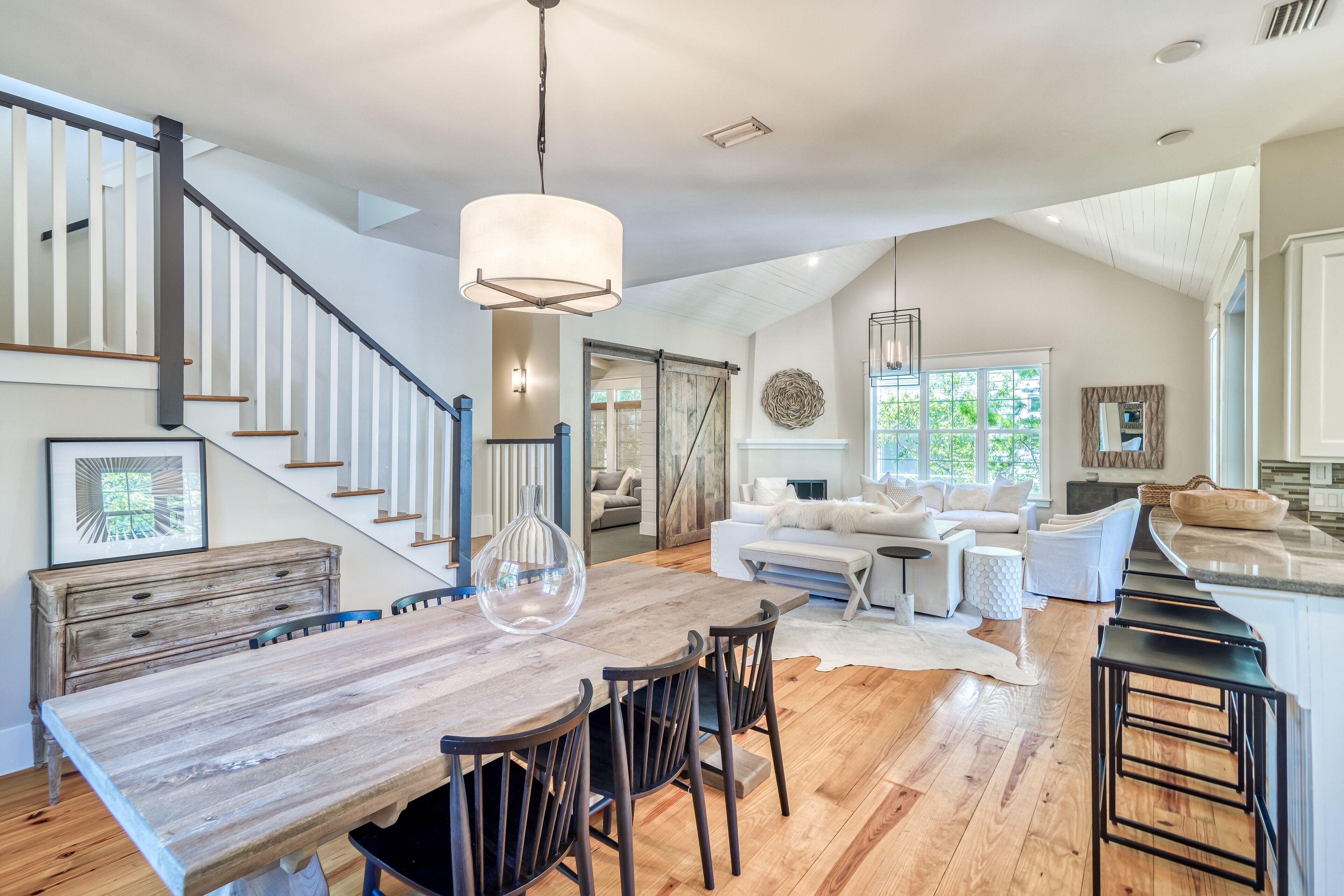 A spacious living area with a wooden dining table, black chairs, a white sofa, and a staircase with white railings.
