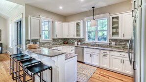 A spacious kitchen with white cabinets, a granite countertop, and a large island with bar stools. - Luxury 2-Story Home | 2-min to pool | 8-min to the beach | 1-mile from Seaside (Seagrove Beach)