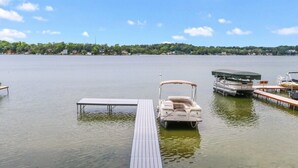 A calm lake with a wooden dock extending into the water, a pontoon boat, and a rowboat.