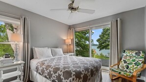 A bedroom with a large bed, a chair, a nightstand, and a view of the outdoors.