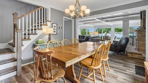 A spacious dining area with a wooden table and chairs, a chandelier, and a staircase leading to another level.