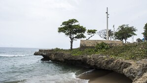 Un paysage côtier avec une falaise rocheuse, un mur de pierre et quelques arbres.