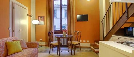 A compact living space with a sofa, a dining table with chairs, a kitchen area, and a staircase.