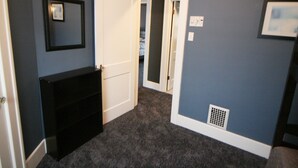 A hallway with a dark carpet, a black console table, and a white door leading to another room. - Safe, Clean & Spacious, Great for Families (Niagara Falls)