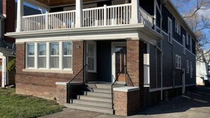 A two-story house with a front porch, a balcony on the upper floor, and a brick facade. - Safe, Clean & Spacious, Great for Families (Niagara Falls)