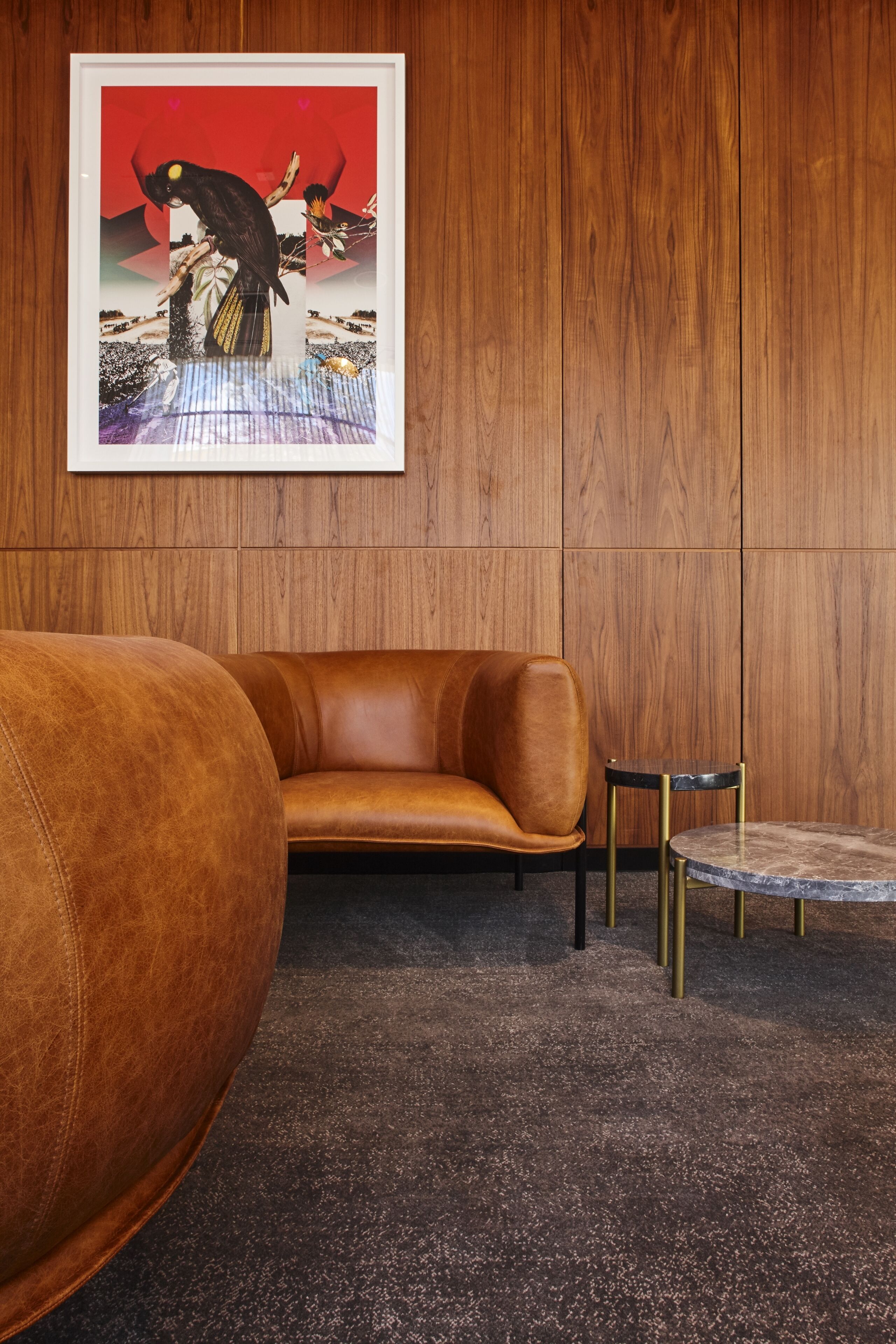 A room with a brown leather sofa, a small round table with a marble top, and a framed artwork on the wall.