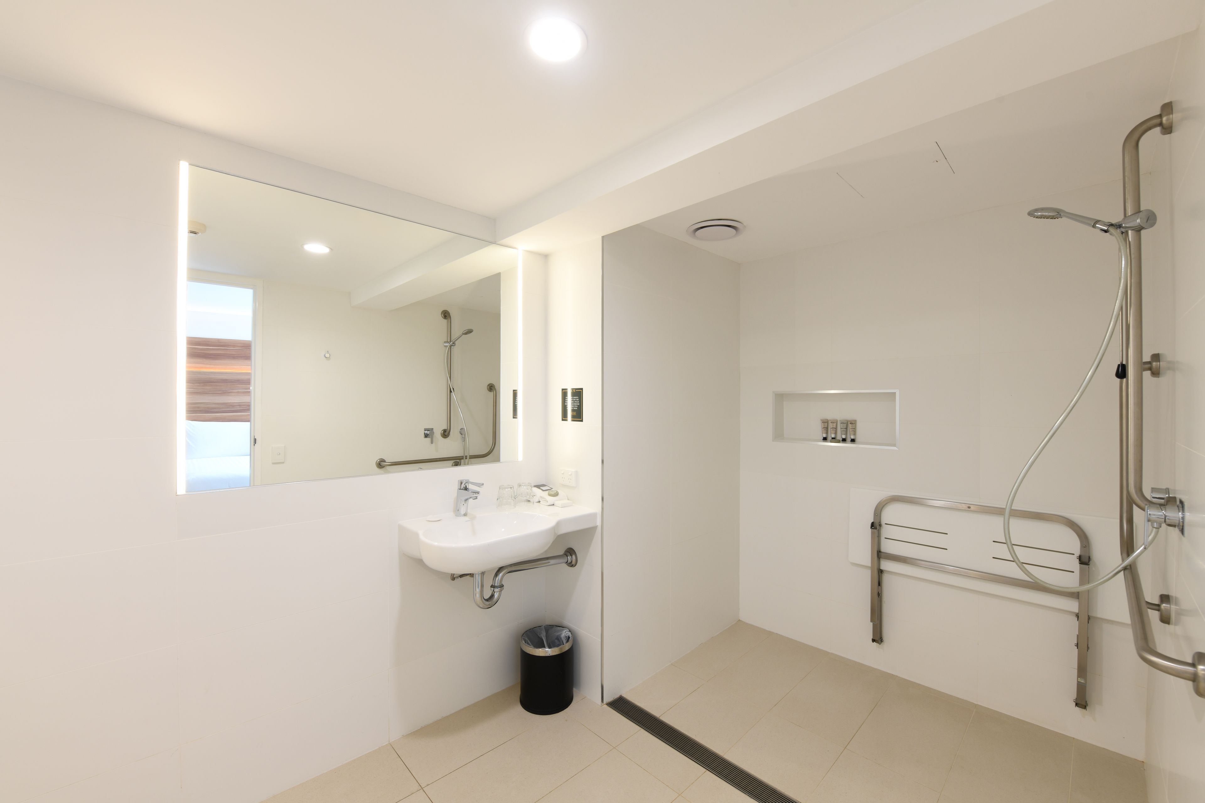 A modern bathroom with a sink, mirror, shower, and a handrail.