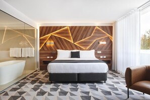 Ett modernt hotellrum med en stor säng, en dusch med glasväggar och ett golv med ett geometriskt mönster.