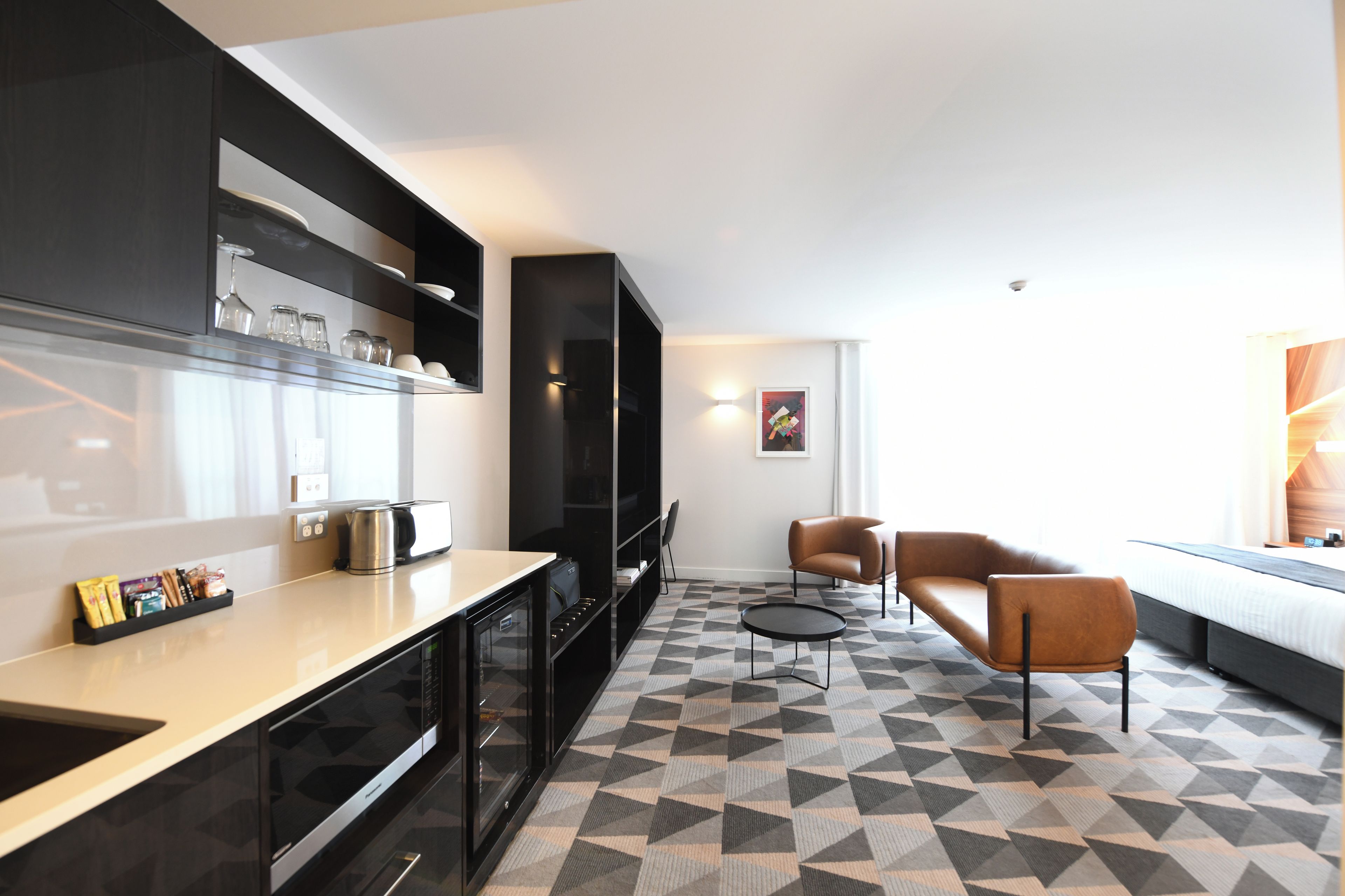 A modern kitchen with a microwave, kettle, and coffee maker. There is a seating area with a sofa and chairs.