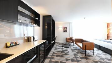 A modern kitchen with a microwave, kettle, and coffee maker. There is a seating area with a sofa and chairs.