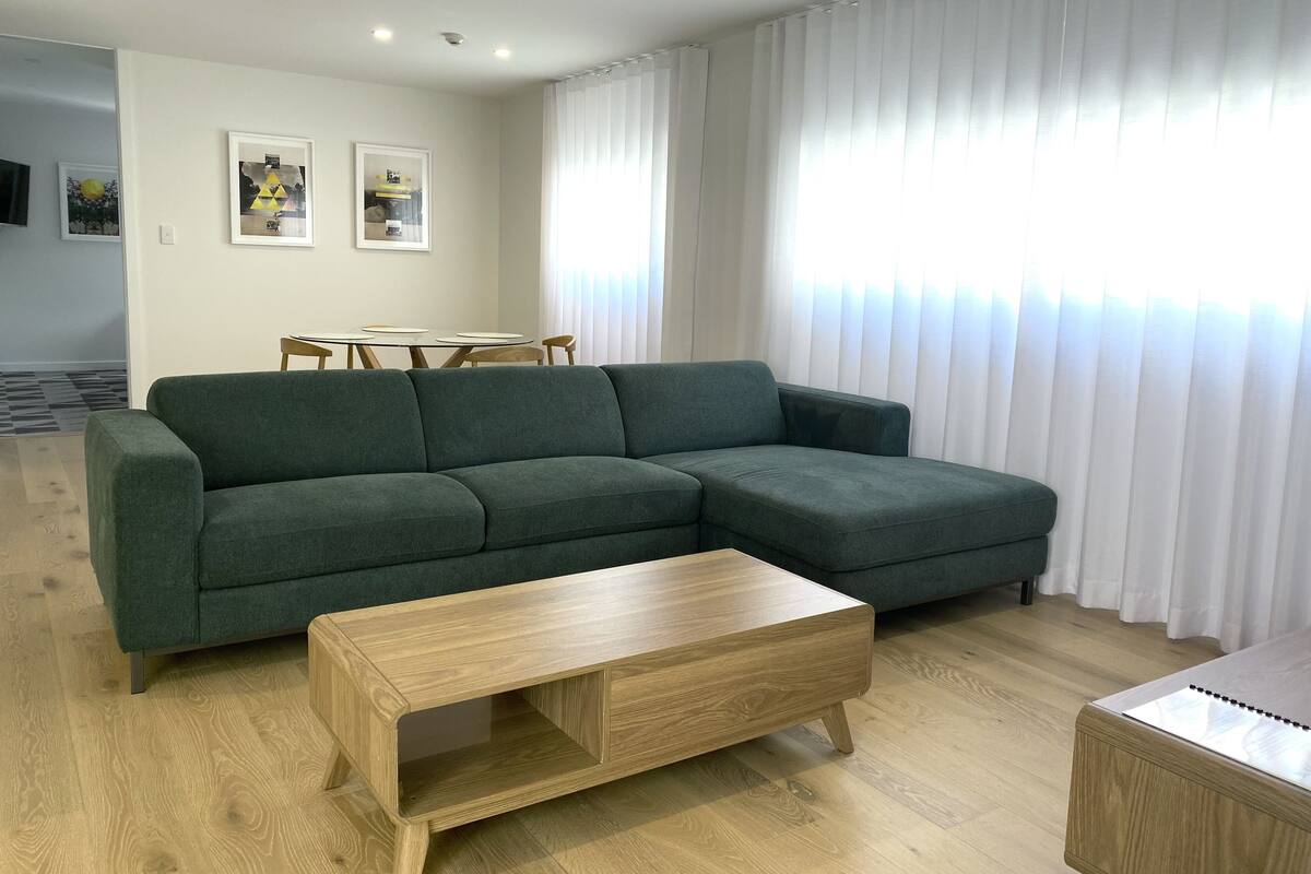 Una sala de estar moderna con un sofá seccional verde, una mesa de centro de madera y un comedor con una mesa pequeña y sillas.