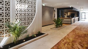 Een moderne hotellobby met een receptiebalie, decoratieve wandpanelen en potplanten.