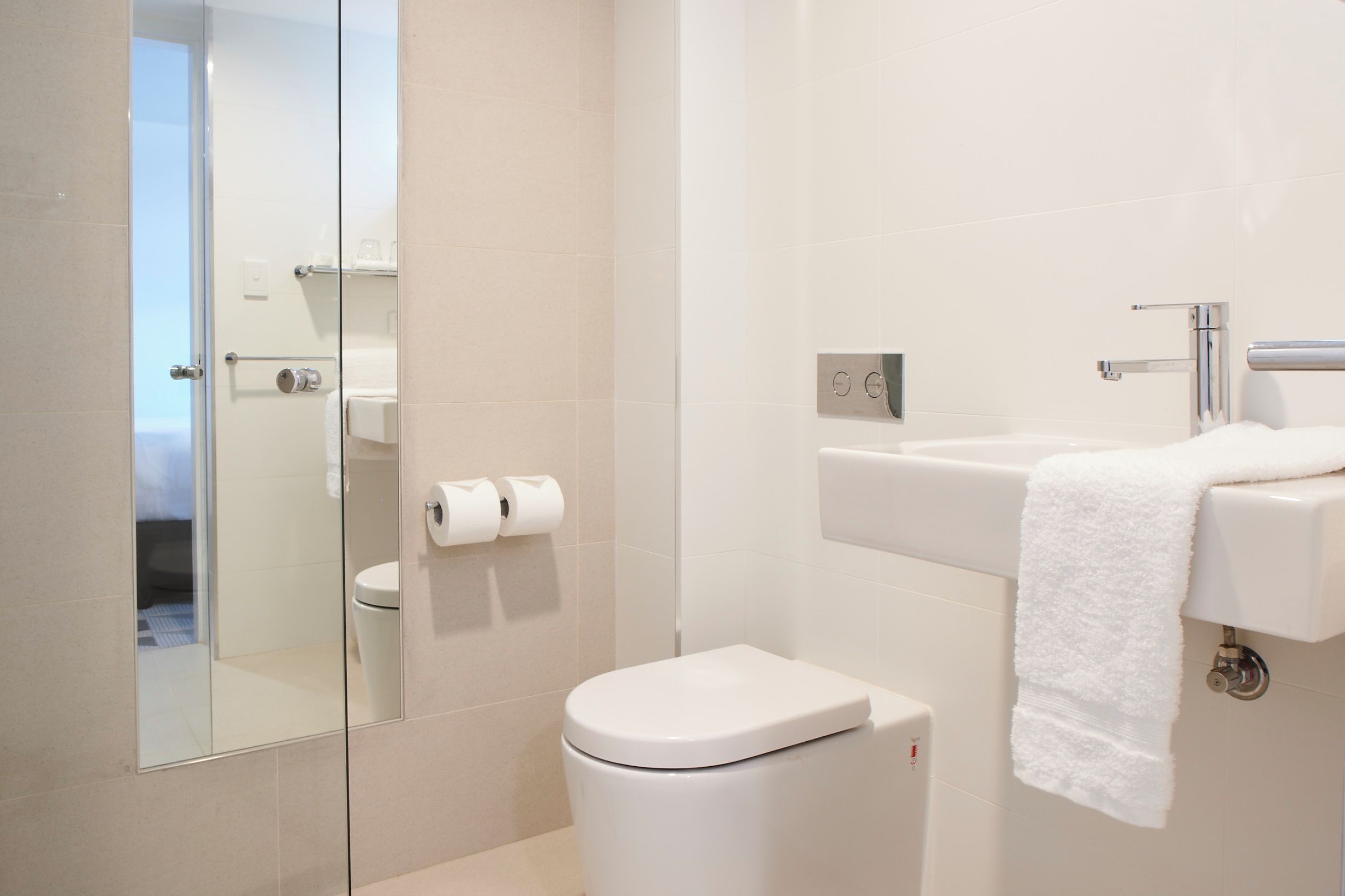 A modern bathroom with a toilet, a glass shower enclosure, and a sink with a towel hanging on the wall.