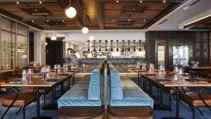 Een restaurant met lange gedeelde tafels, blauwe kussensbanken en een bar in het midden.