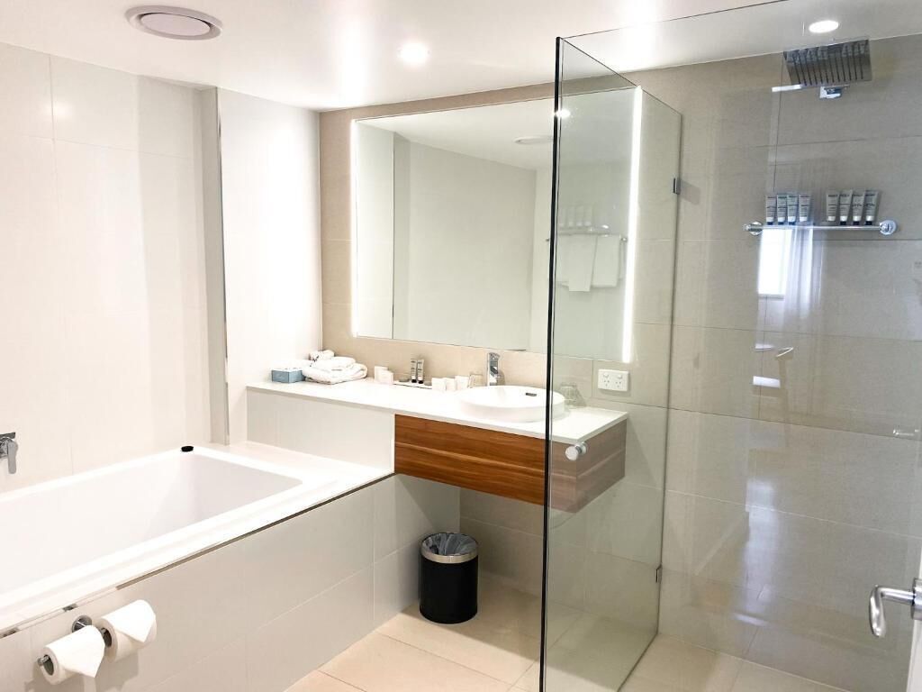 Un baño moderno con ducha de mampara de vidrio, un lavabo blanco y un espejo grande.