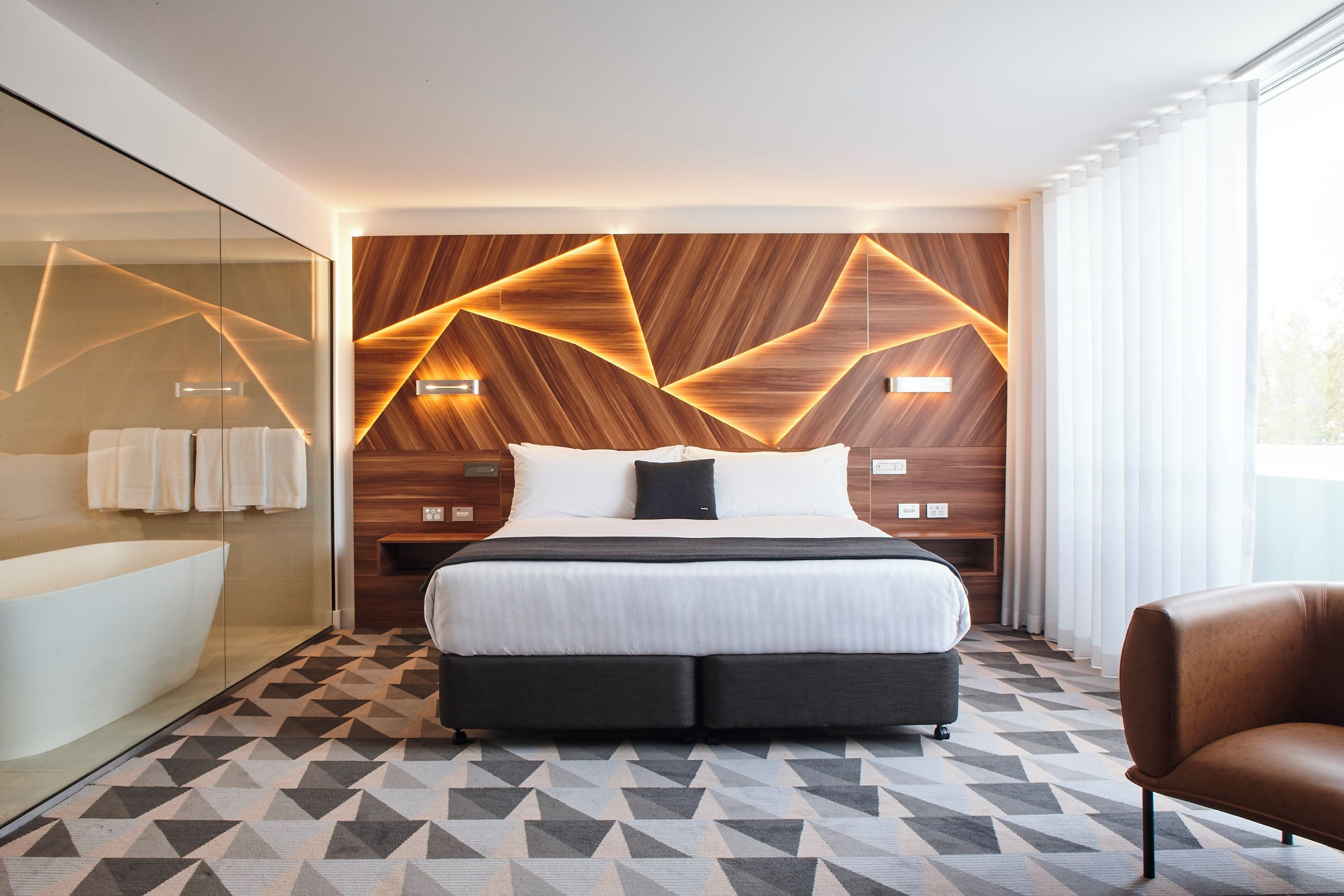 Ett modernt hotellrum med en stor säng, en dusch med glasväggar och ett golv med ett geometriskt mönster.