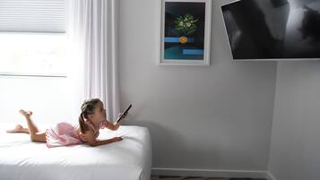 A child lying on a bed with a smartphone, a framed picture on the wall, and a television mounted on the wall.